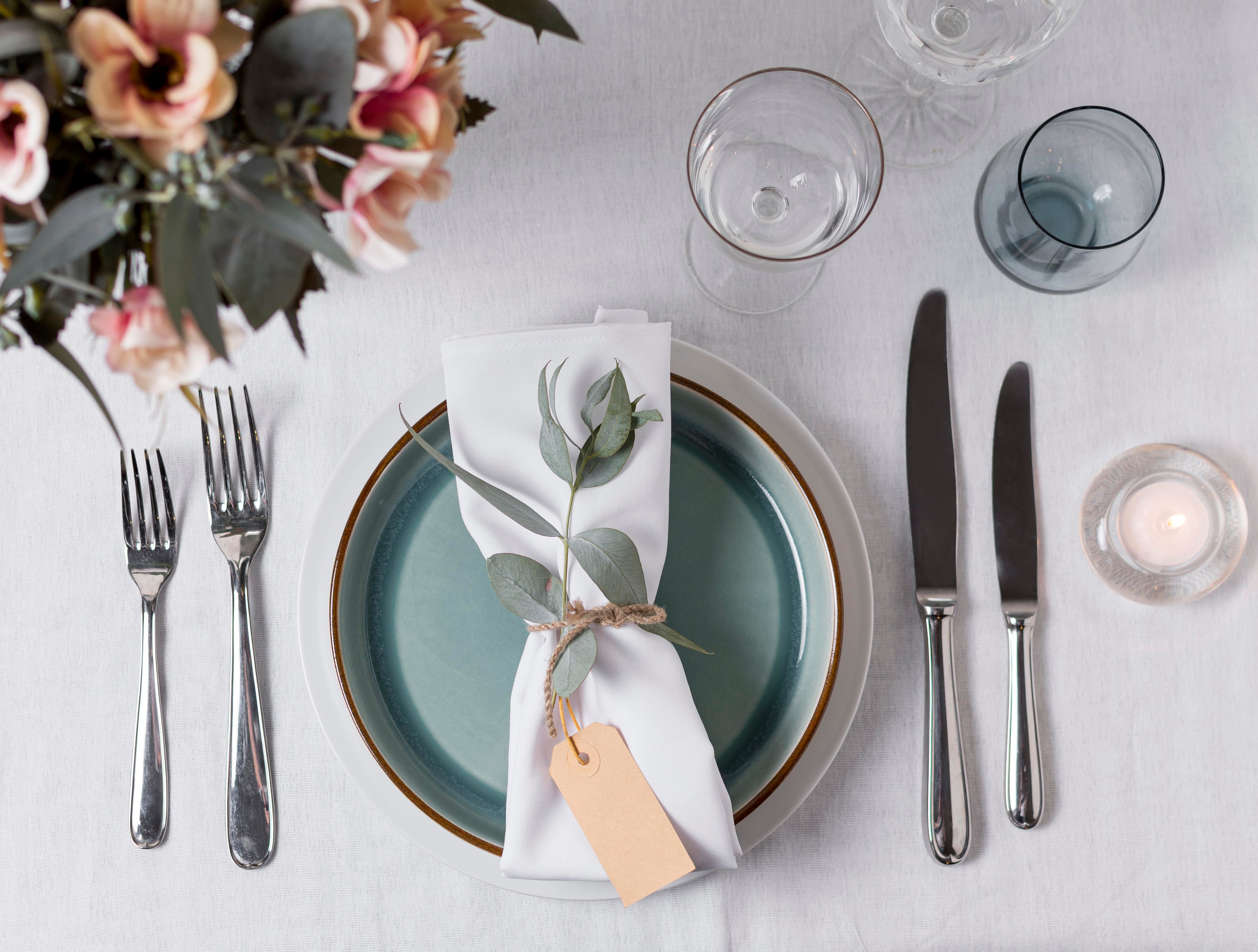 Elegant table setting with flowers, plates, cutlery, and glasses on a white tablecloth.