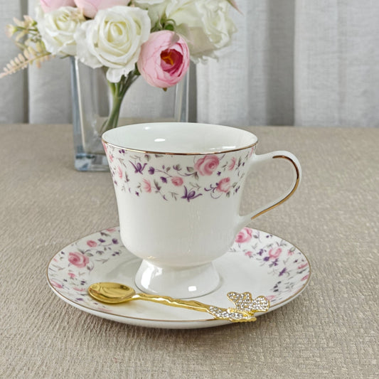 Floral teacup and saucer set on a table with a vase of flowers in the background